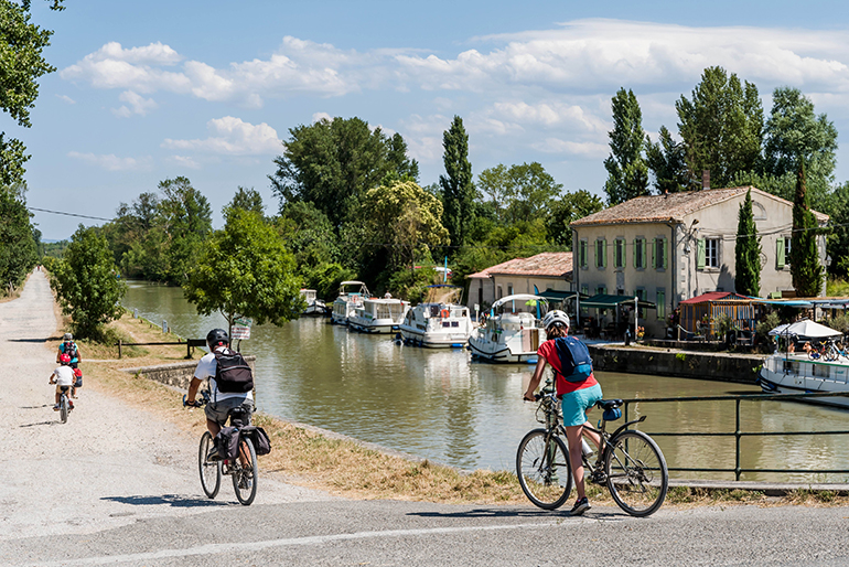 Personnes faisant du vélo le long du canal du Midi devant un bâtiment de VNF